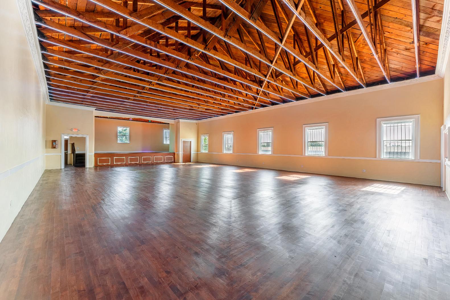 An event venue hall with exposed wooden beams, large windows, and polished hardwood floors at Grand Lodge of LA.