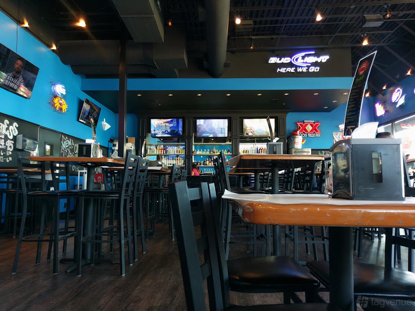 A restaurant with high-top tables, black chairs, blue walls, and multiple TVs at Shell Shack Plano.