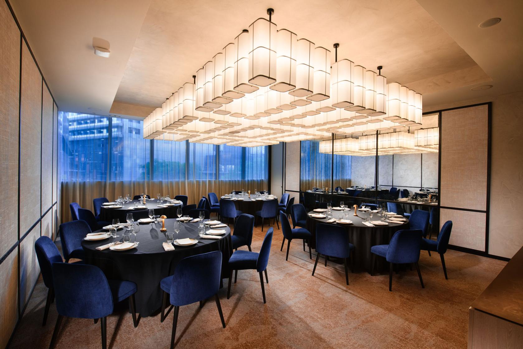 A hotel meeting room with round tables, navy chairs, and geometric ceiling lights at Dorsett Melbourne.