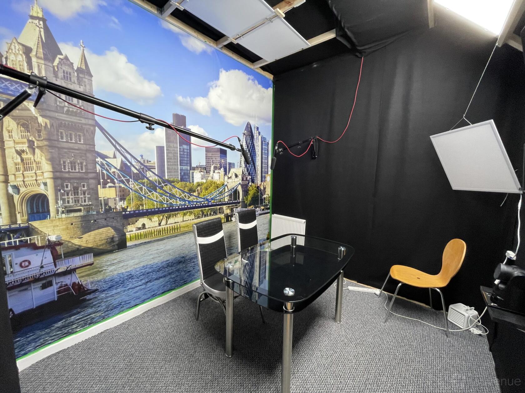A recording studio with a glass table, three black chairs, and a London cityscape mural at TMH Studios.