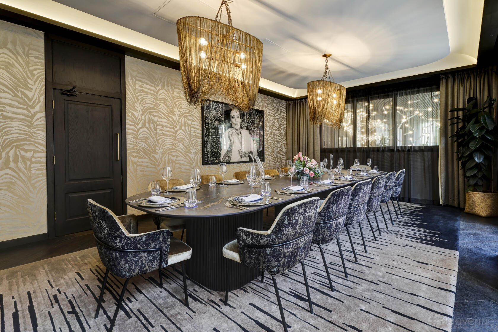 A dining room with a long oval table, velvet chairs, woven pendant lights, and patterned carpet at AMANO Hotel Covent Garden.