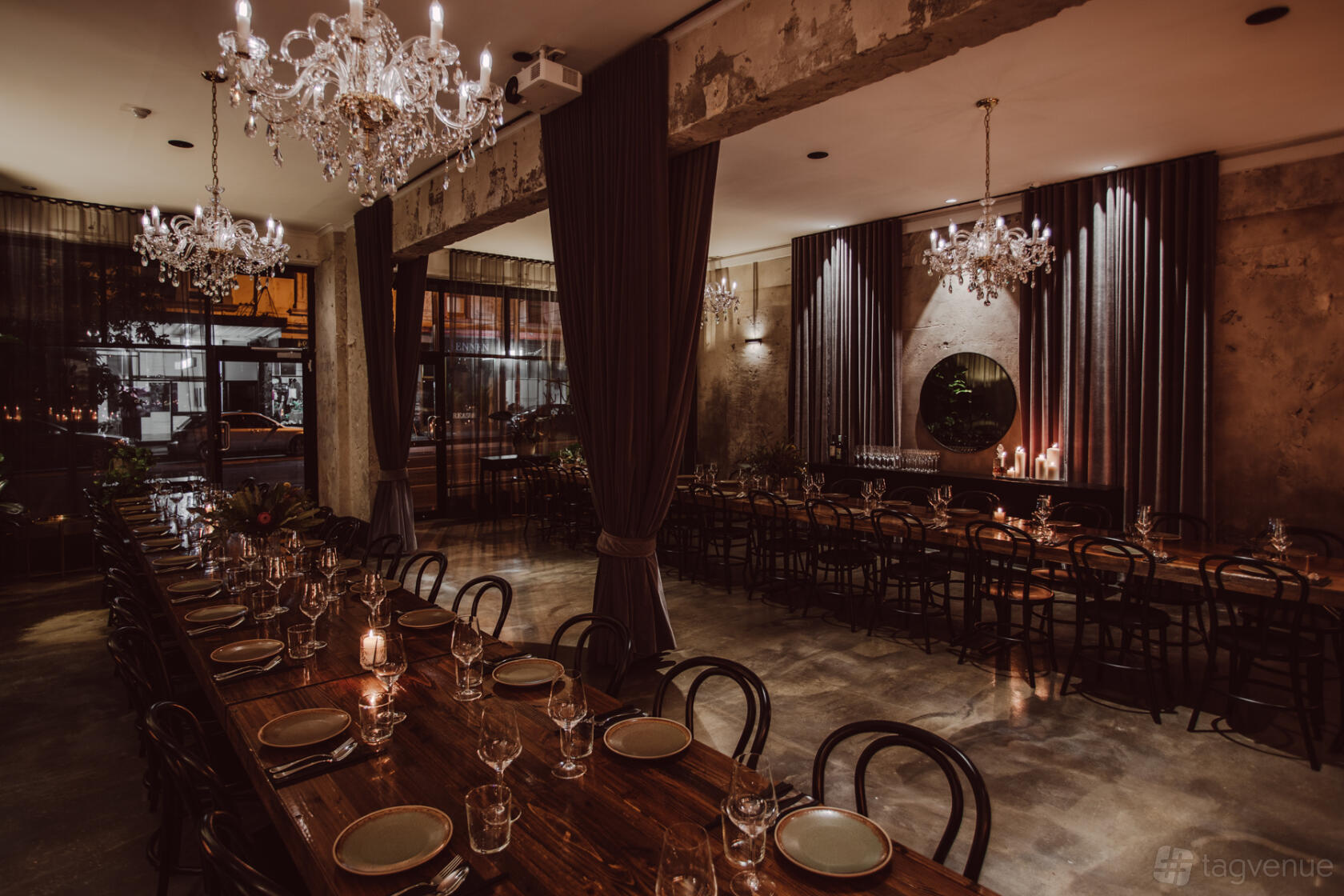 An event venue with long wooden tables, elegant chandeliers, and draped curtains at Aunty Kim's.