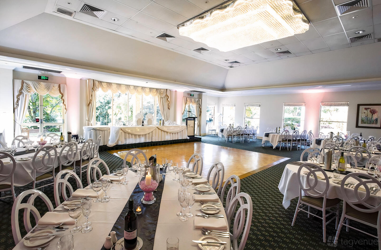 A country house ballroom with round tables, white chairs, a dance floor, and large windows at Linton Gardens.