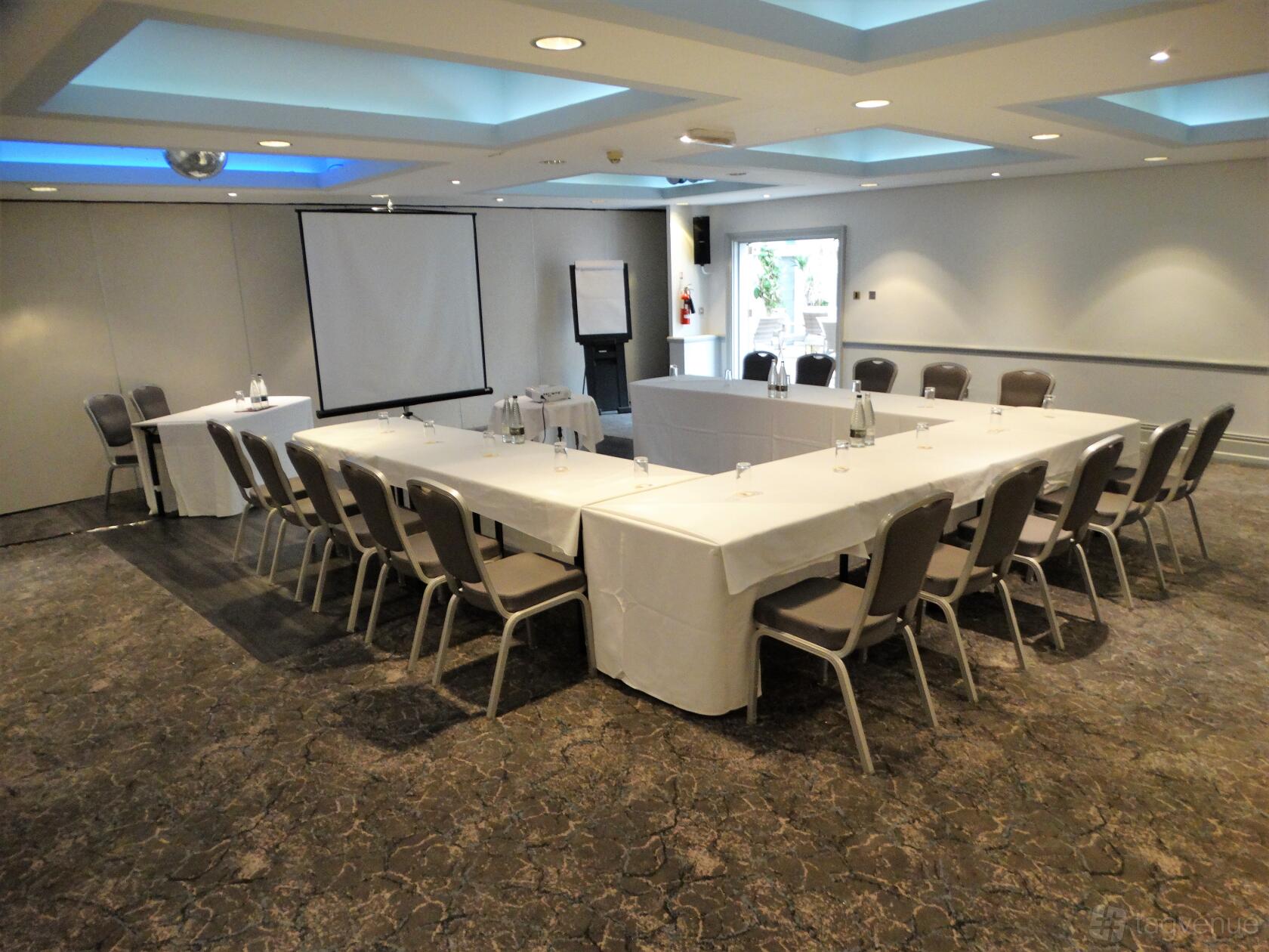 An event space with U-shaped tables, grey chairs, and a projector screen at Nailcote Hall Hotel.