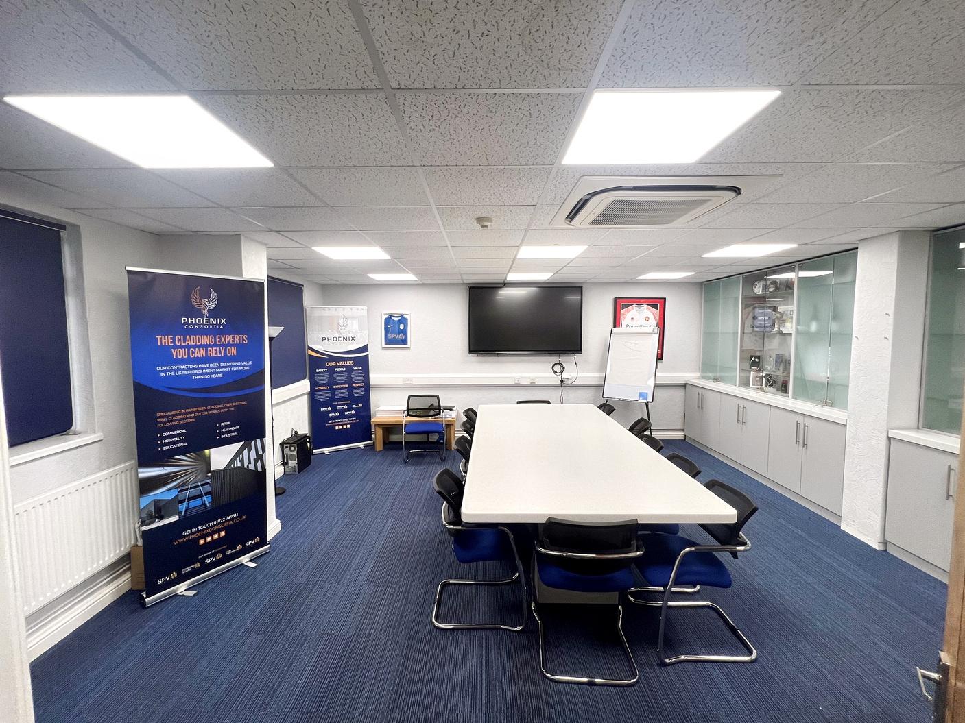 A training room with a rectangular table, black chairs, a large wall-mounted screen, and display cabinets at SPV Training Facilities.