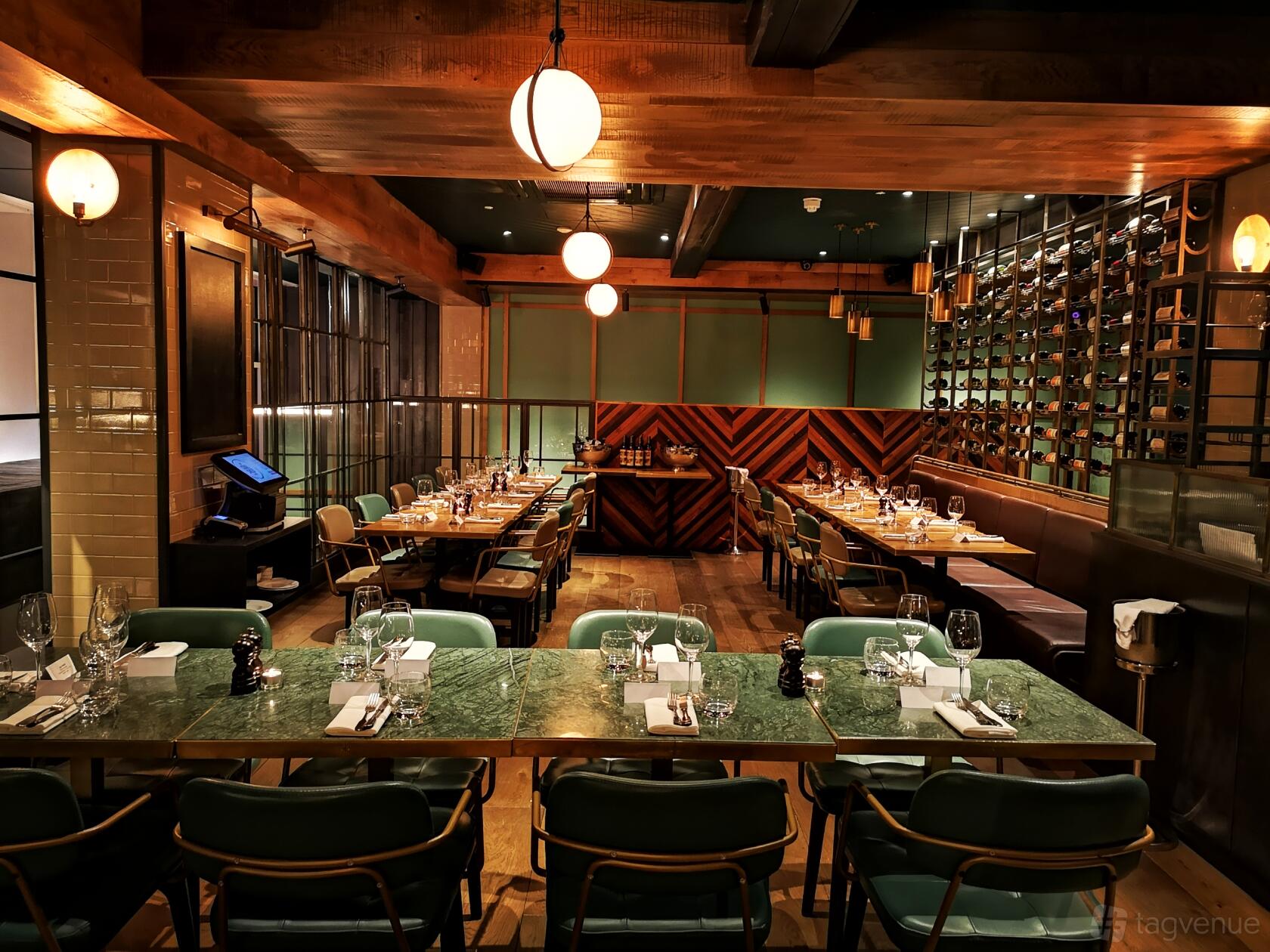 A dining room with green marble tables, wine wall, and pendant lighting at The Coal Shed- London.