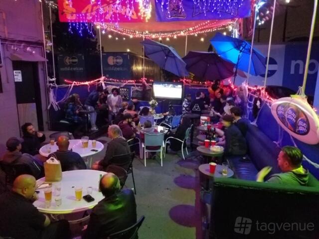 A terrace bar with outdoor seating, round tables, umbrellas, and string lights at The Blue Moon Lounge.