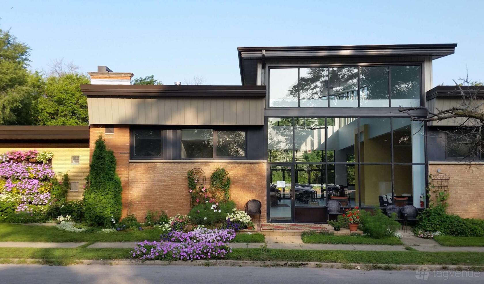A versatile event space with floor-to-ceiling windows, brick exterior, and blooming garden at Wild Blossom Meadery & Winery.
