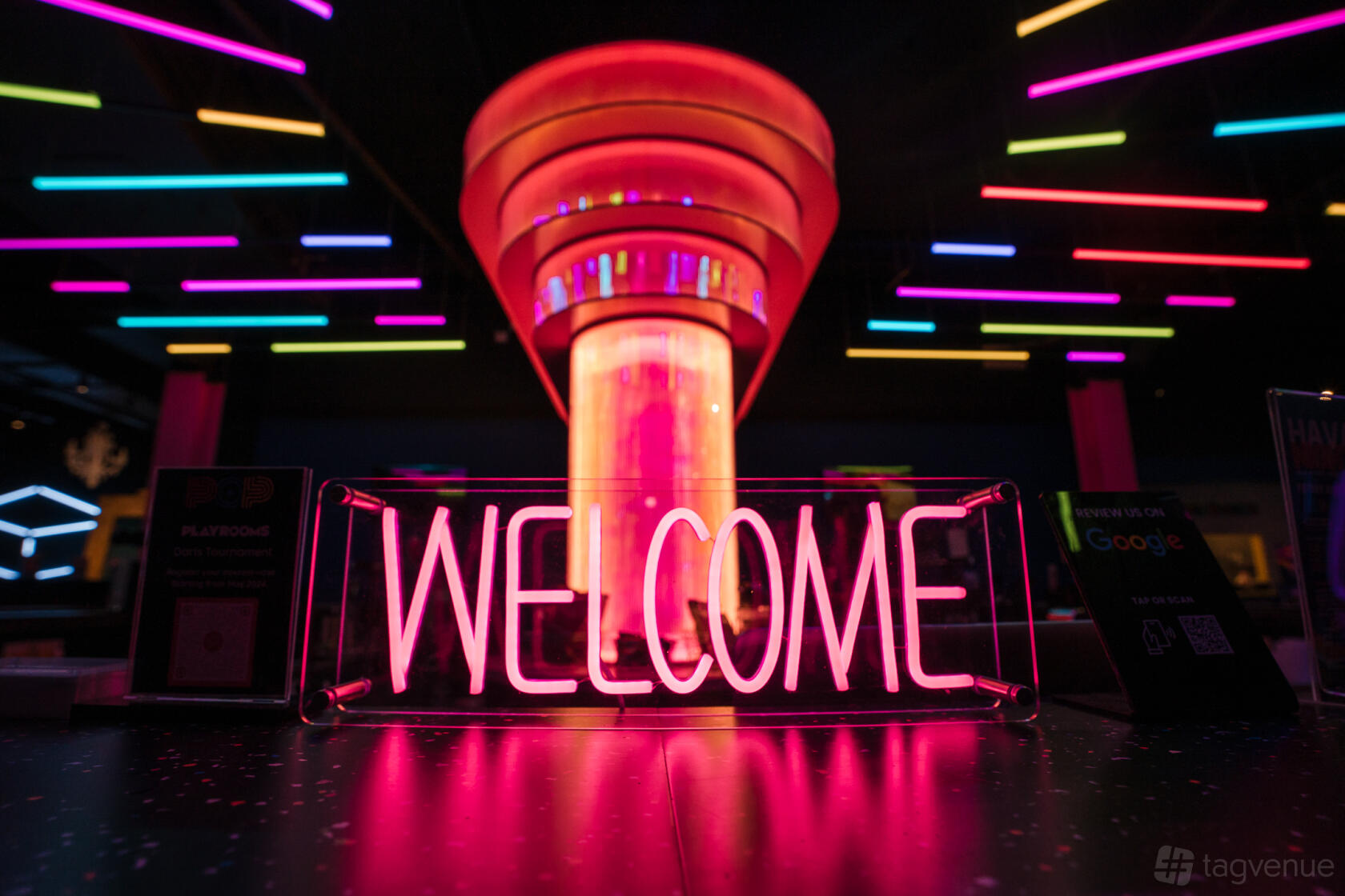 An event venue with neon lighting, a glowing welcome sign, and colorful illuminated ceiling fixtures at Pop Playrooms.