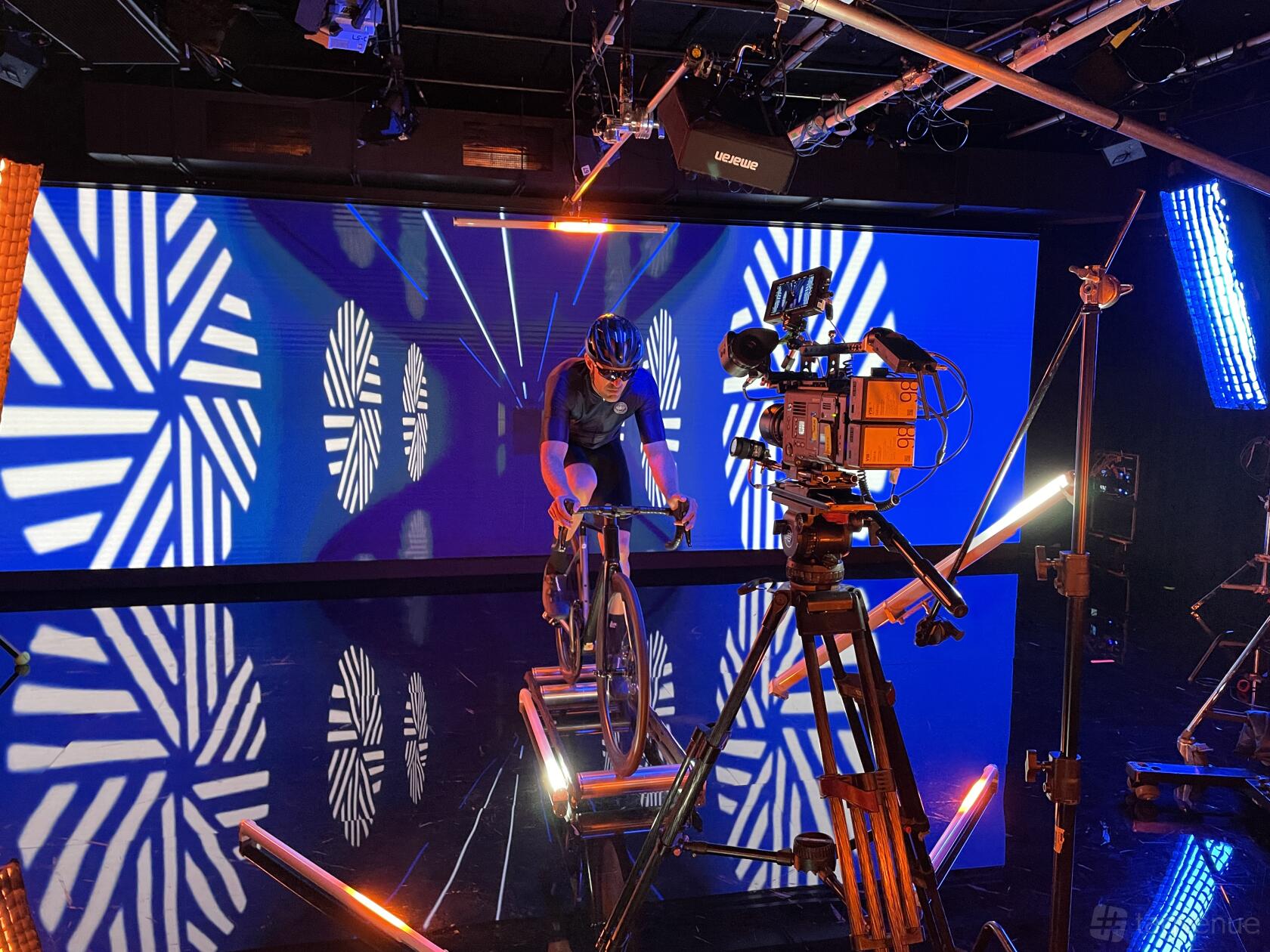 A TV studio with a cyclist on stationary rollers, LED stage lights, and a large digital video wall at Gravity Media Production Centre Sydney.