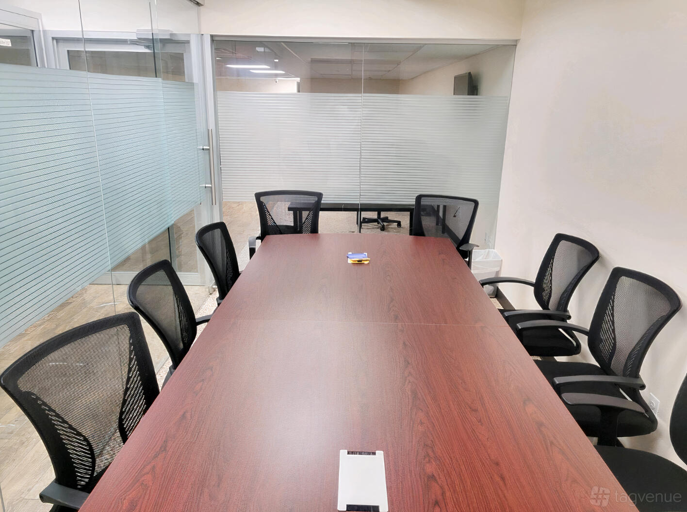 A coworking meeting room with a long wooden table, black mesh chairs, and floor-to-ceiling glass walls at Absolute Spaces.