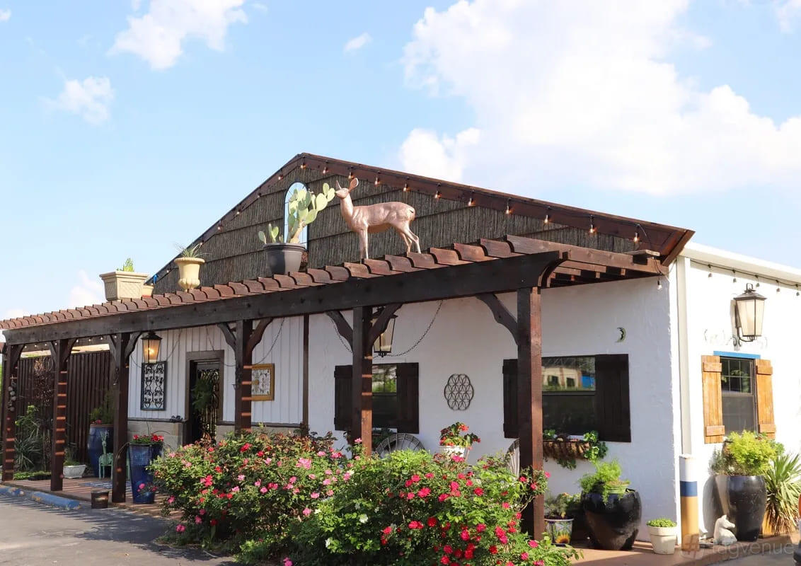 A versatile event space with a wood pergola entrance, potted plants, and a deer sculpture at Azle Deer Cove.