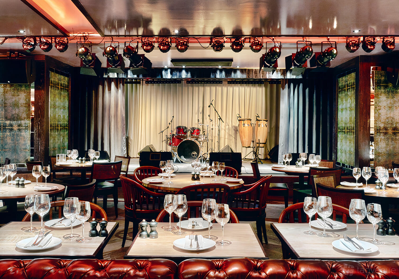 A restaurant with a live music stage, drum kit, spotlighting, and tables set with glassware at 100 Wardour Street.