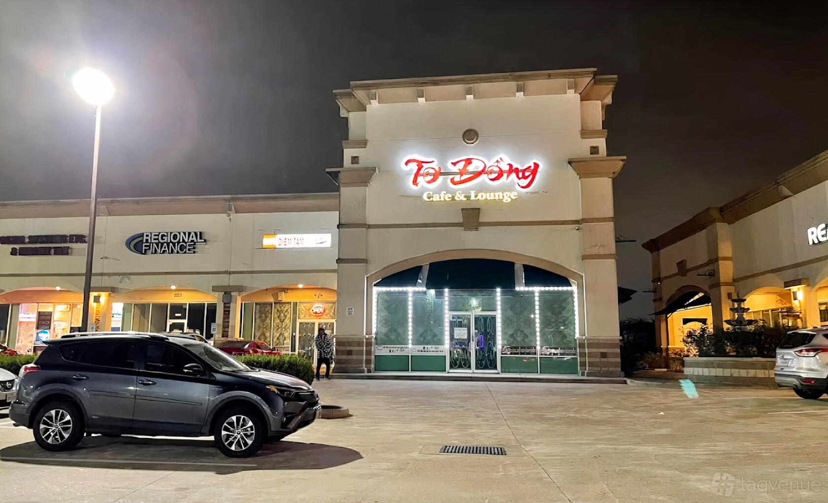 A restaurant exterior with illuminated signage, large windows, and parking spaces at To Dong Restaurant.