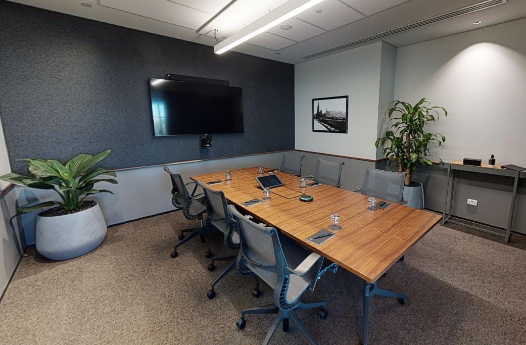 A coworking space with a conference table, mesh chairs, wall-mounted screen, and indoor plants at Hub Flinders Street.