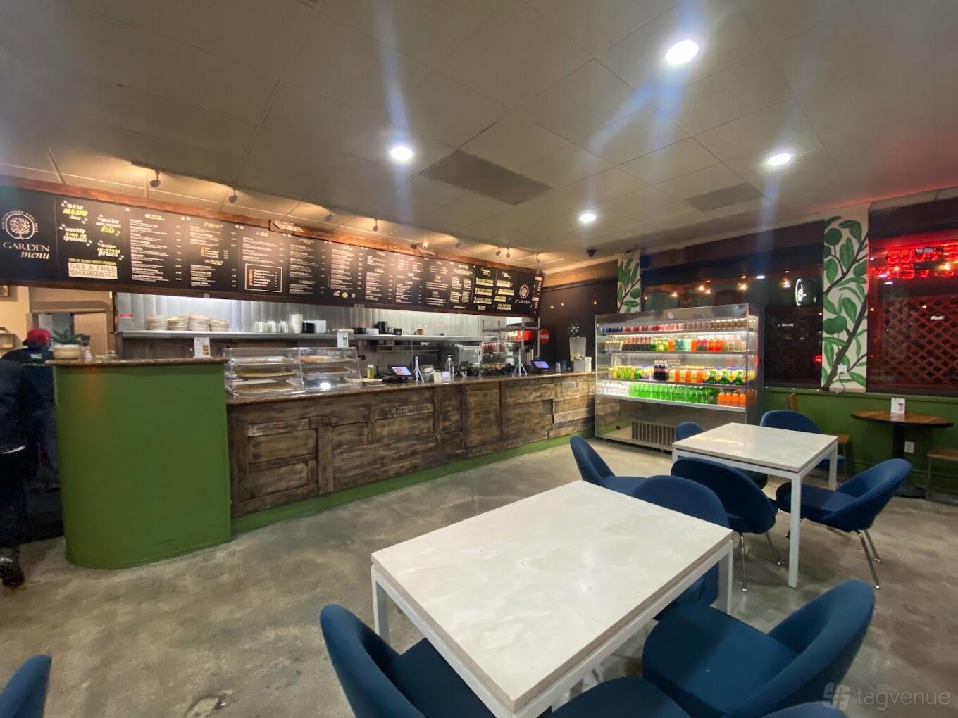 A restaurant dining area with white marble tables, blue chairs, a rustic wood counter, and a menu board at Z Garden Mediterranean Cuisine.