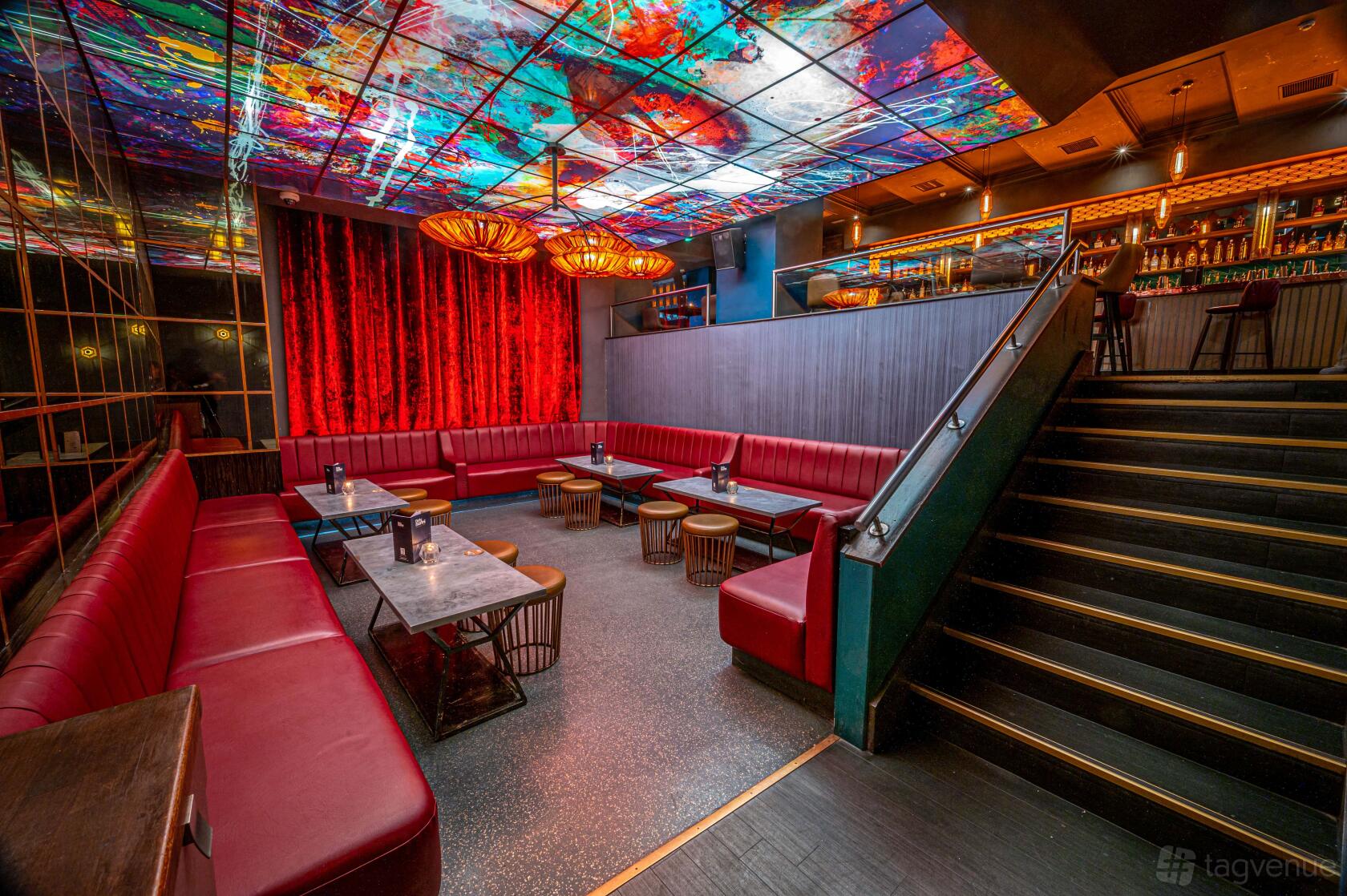 An event space with red leather banquettes, marble tables, and a colorful mirrored ceiling at Dirty Martini St. Paul's.
