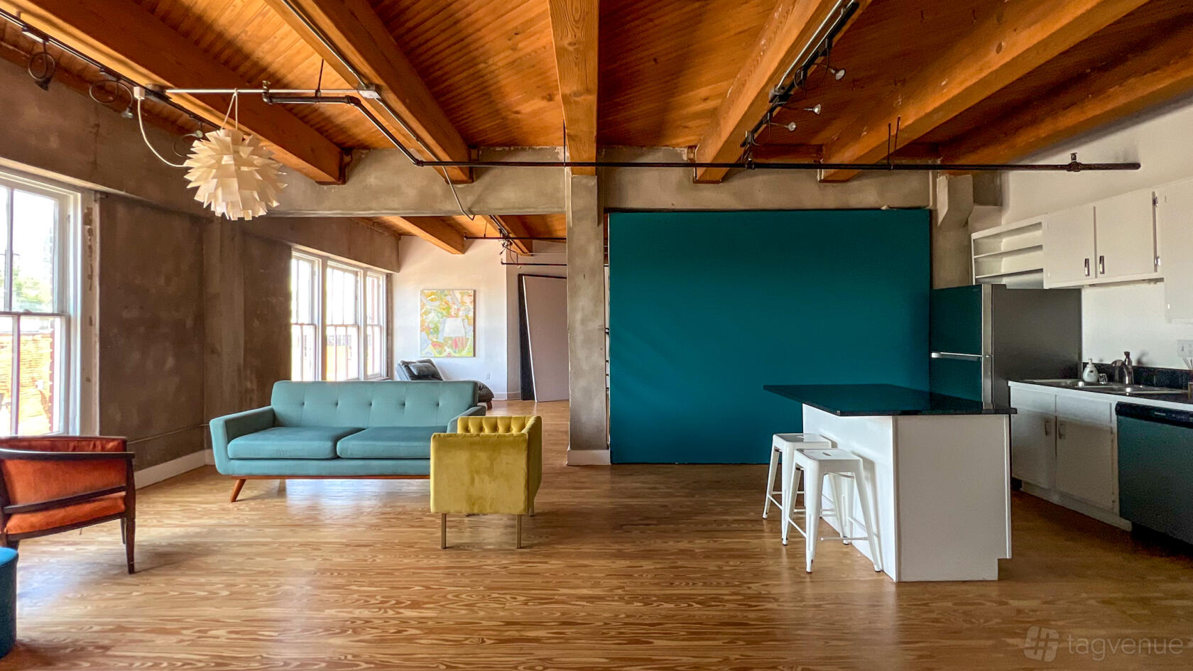 A photo studio with exposed wood beams, teal backdrop, natural light, and mid-century furniture at NEGATIVE SPACE RENTALS.