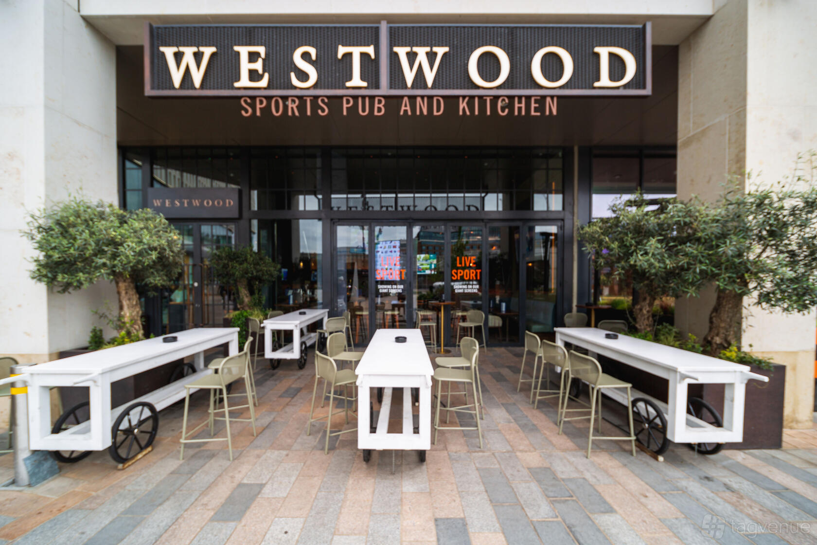 A pub with outdoor seating, white wooden tables, and potted trees at Westwood.