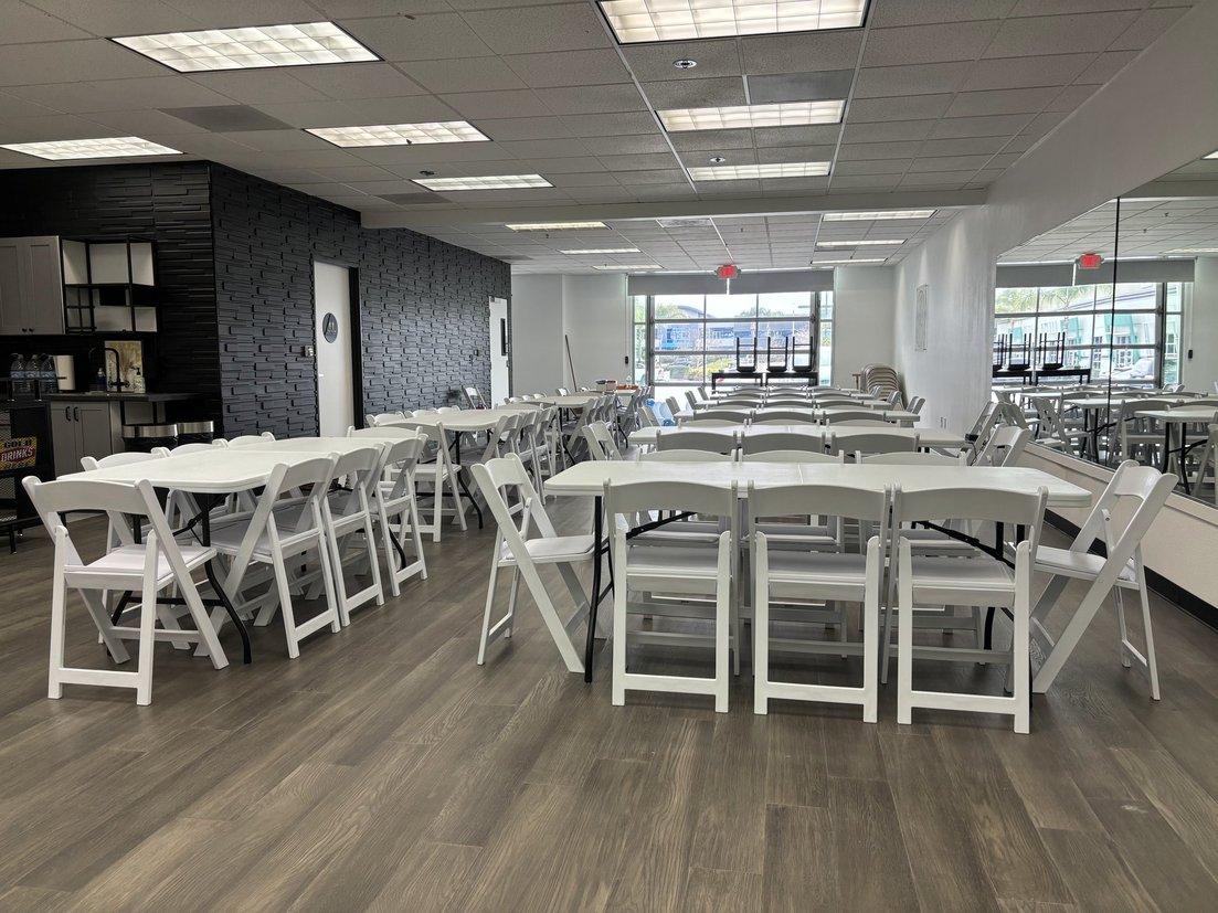 An event space with white folding chairs, rectangular tables, wood flooring, and a black brick accent wall at Gather SD.