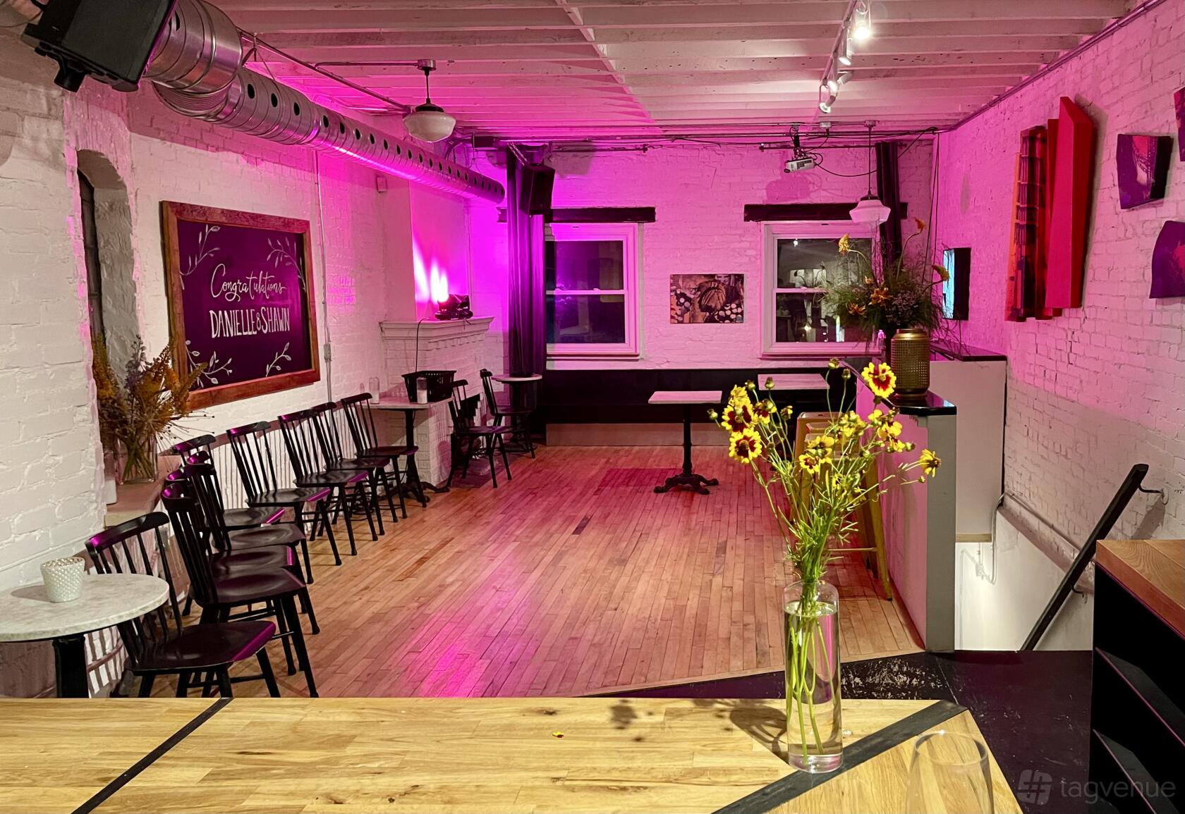 A dining room with wooden floors, exposed white brick walls, and magenta lighting at Bar Neon.
