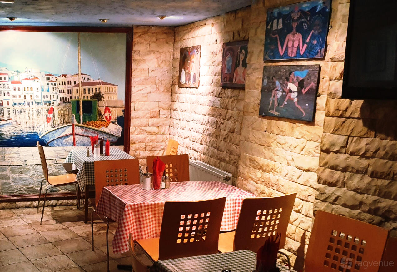 An event space in a restaurant with stone walls, checked tablecloths, and wall art at Bouzouki By Night.