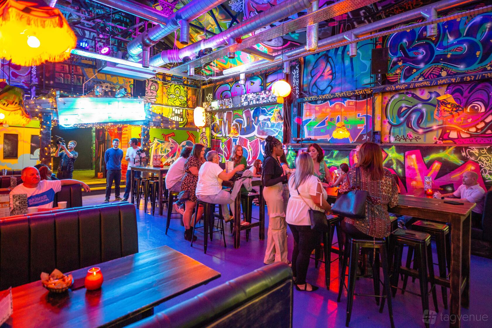 An event venue with vibrant graffiti-covered walls, neon lighting, and high-top tables at Golf Fang Liverpool.