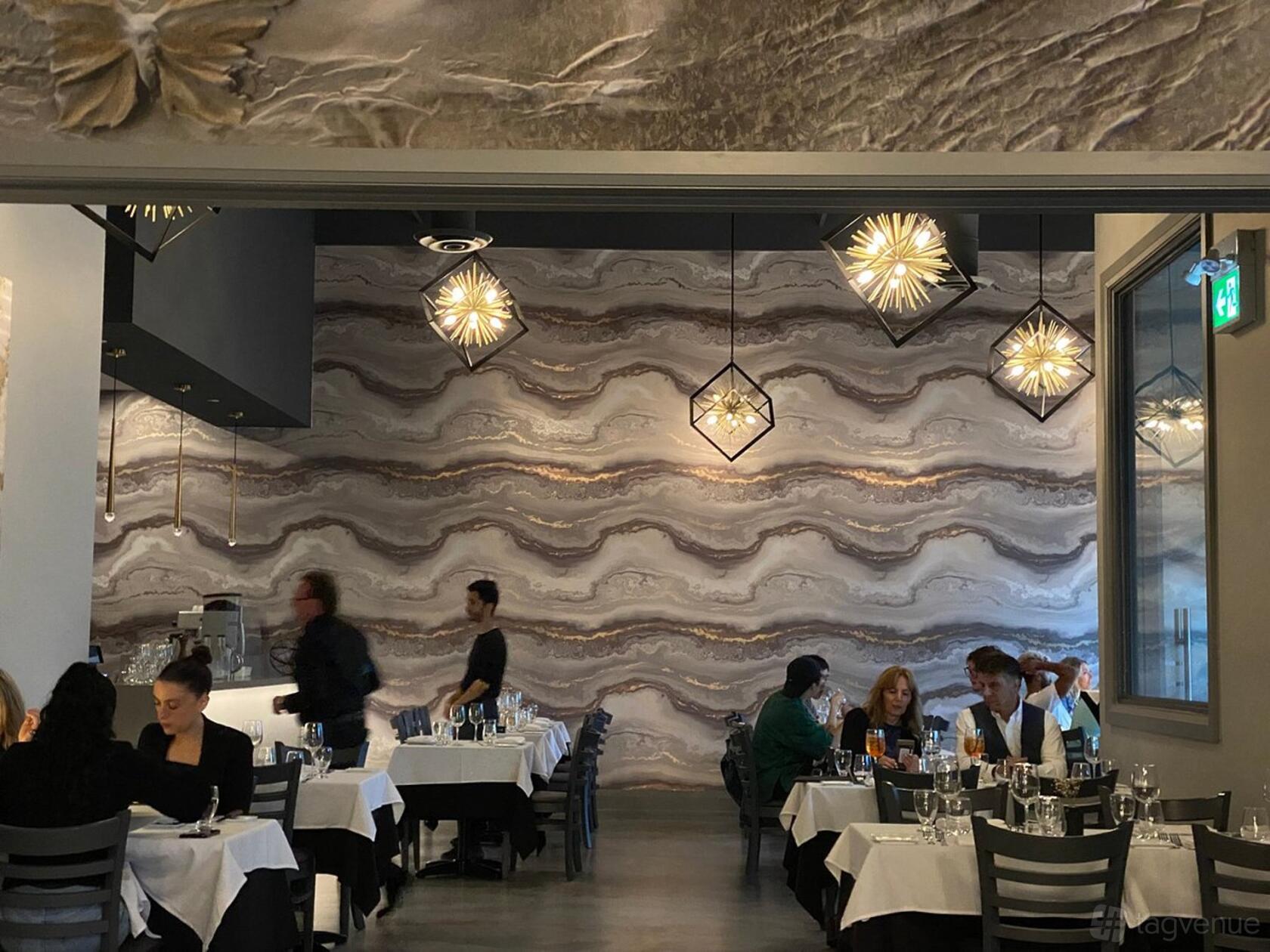 A dining room with patterned stone accent walls, geometric pendant lights, and white-clothed tables at Trimani Ristorante.