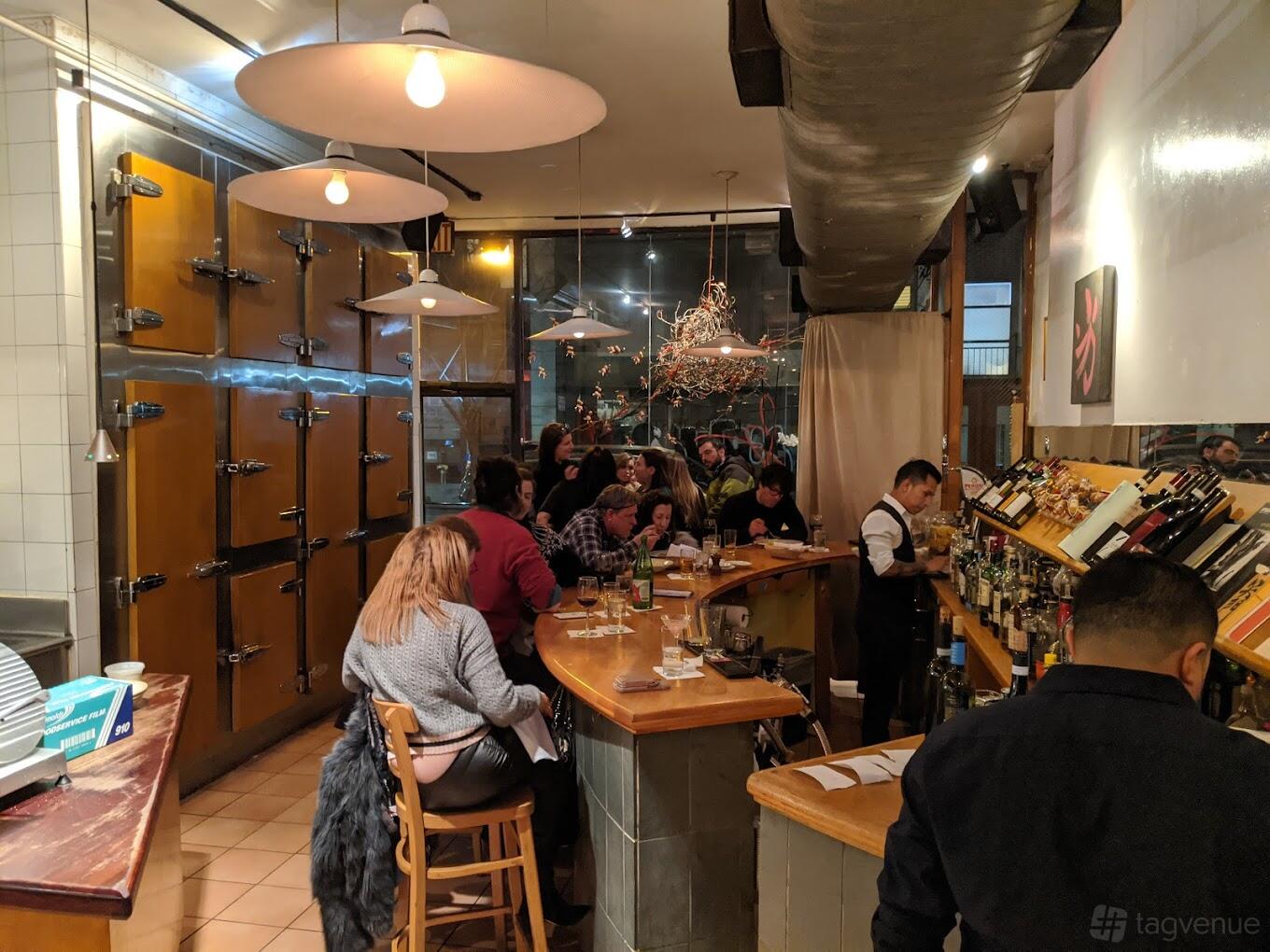 A restaurant with a curved wooden bar, hanging pendant lights, and wall-mounted wine racks at Basta Pasta.