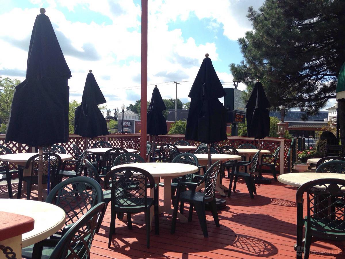 An outdoor restaurant patio with round tables, green chairs, and closed black umbrellas at Great Escape Restaurant.