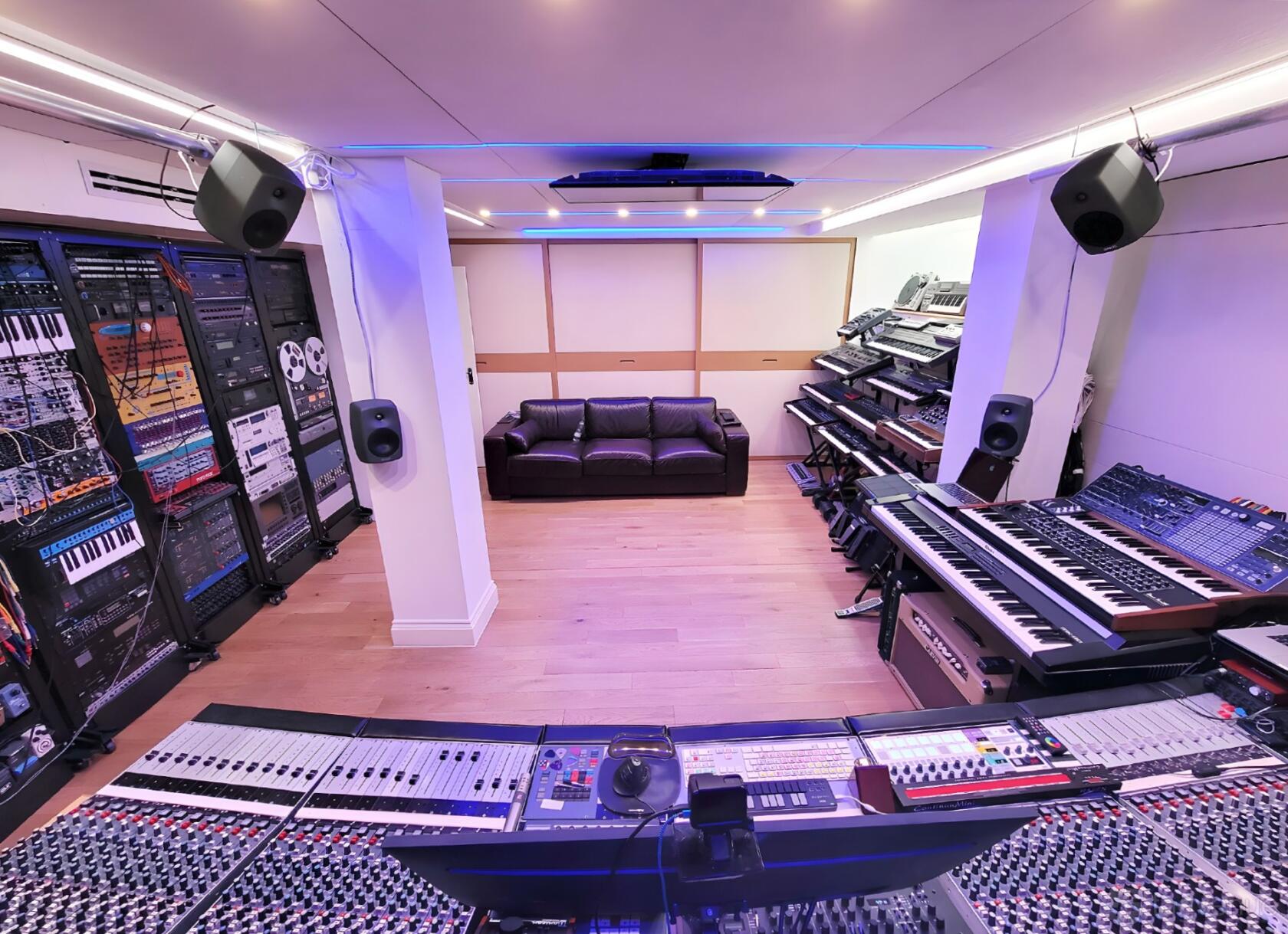 A recording studio with mixing consoles, synthesizers, sound equipment, and a leather sofa at Nevo Sound Studio.