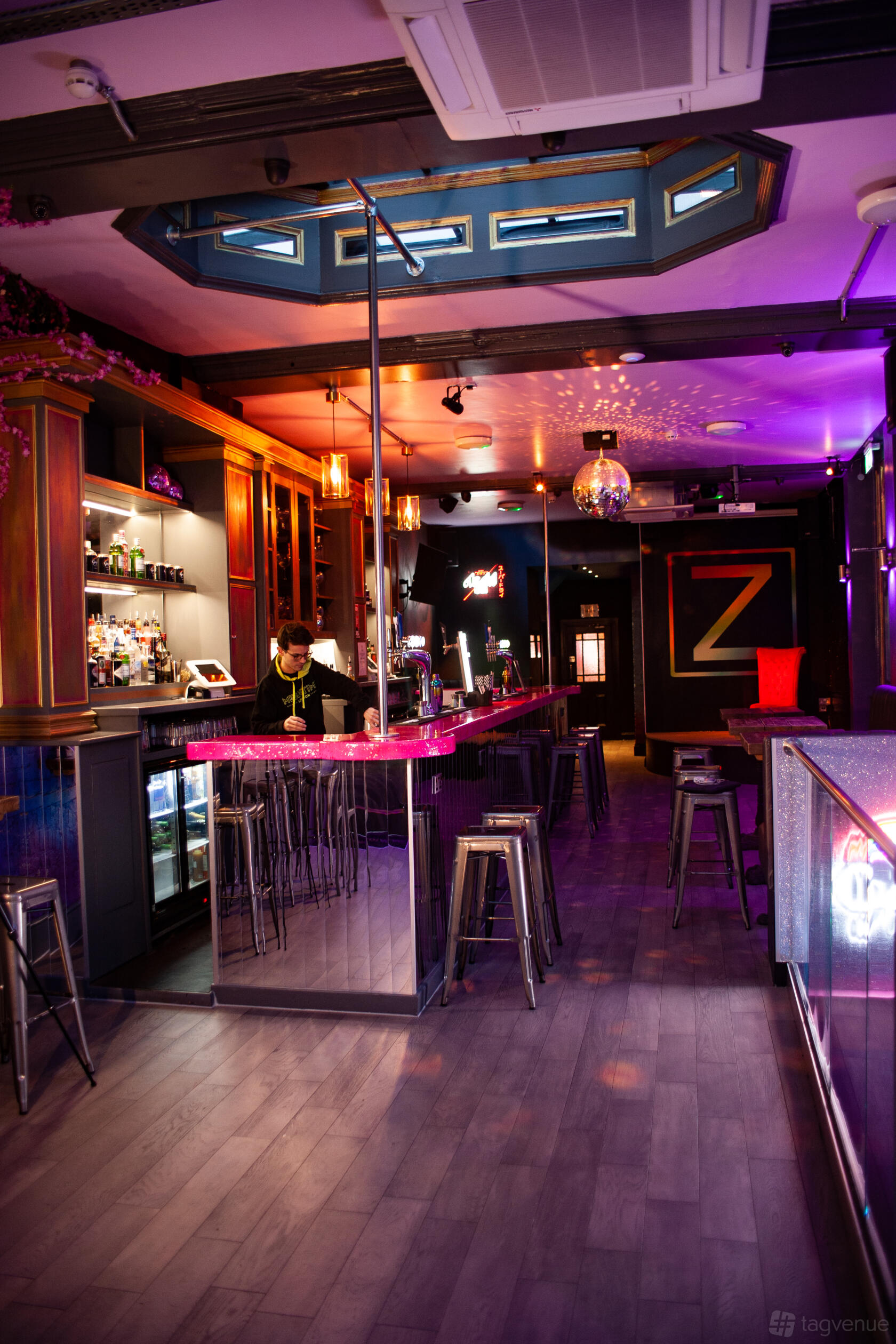 A nightclub with a neon-lit bar, high metal stools, disco ball, and illuminated shelves at ZODIAC Karaoke Bar & Club.