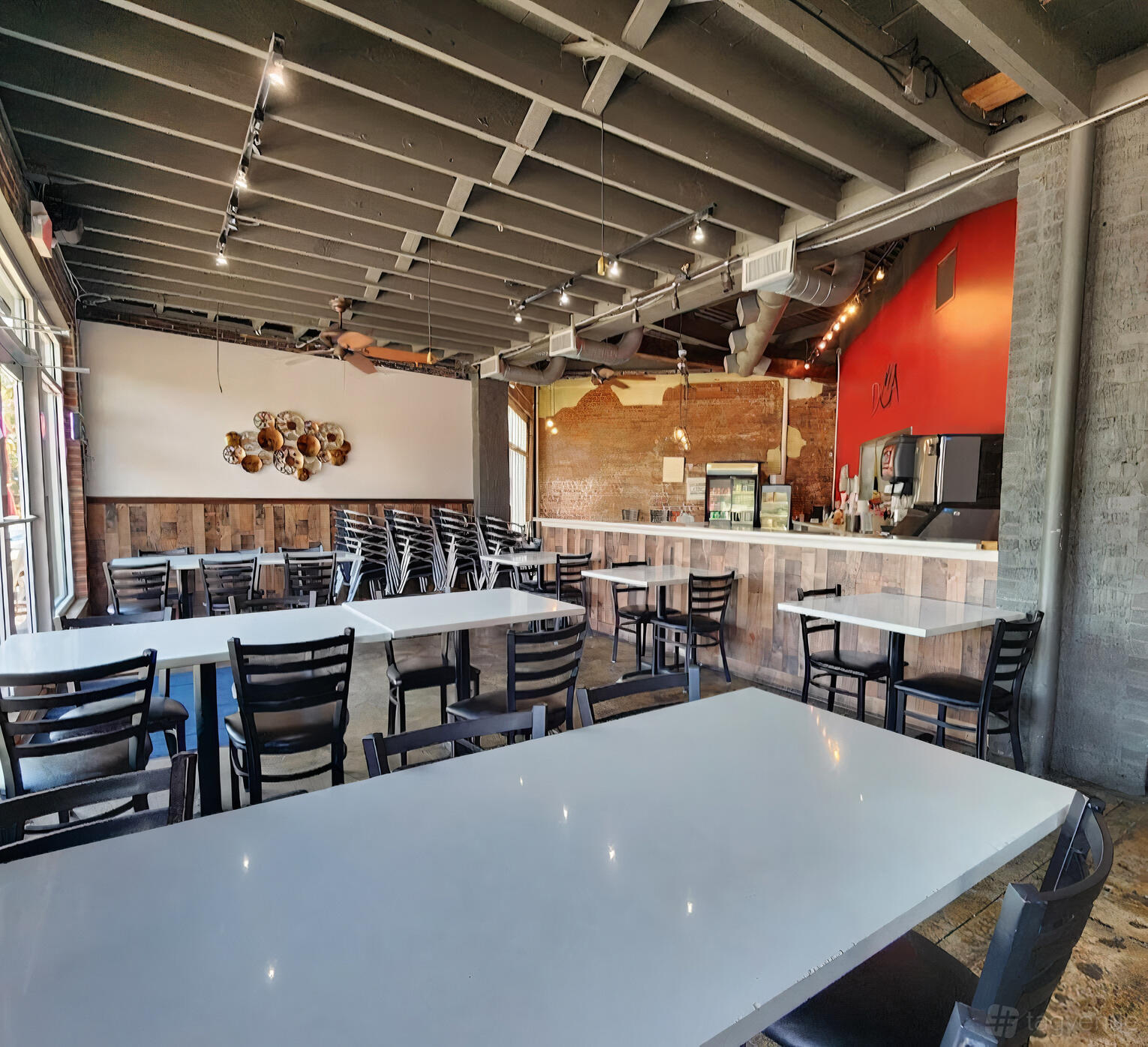 A restaurant with exposed ceiling beams, white tables, and a counter with a drink station at Dua Hapeville.