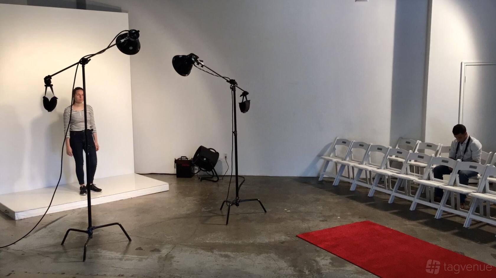 A photo studio meeting room with a small stage, lighting equipment, and white folding chairs at Select Studios.