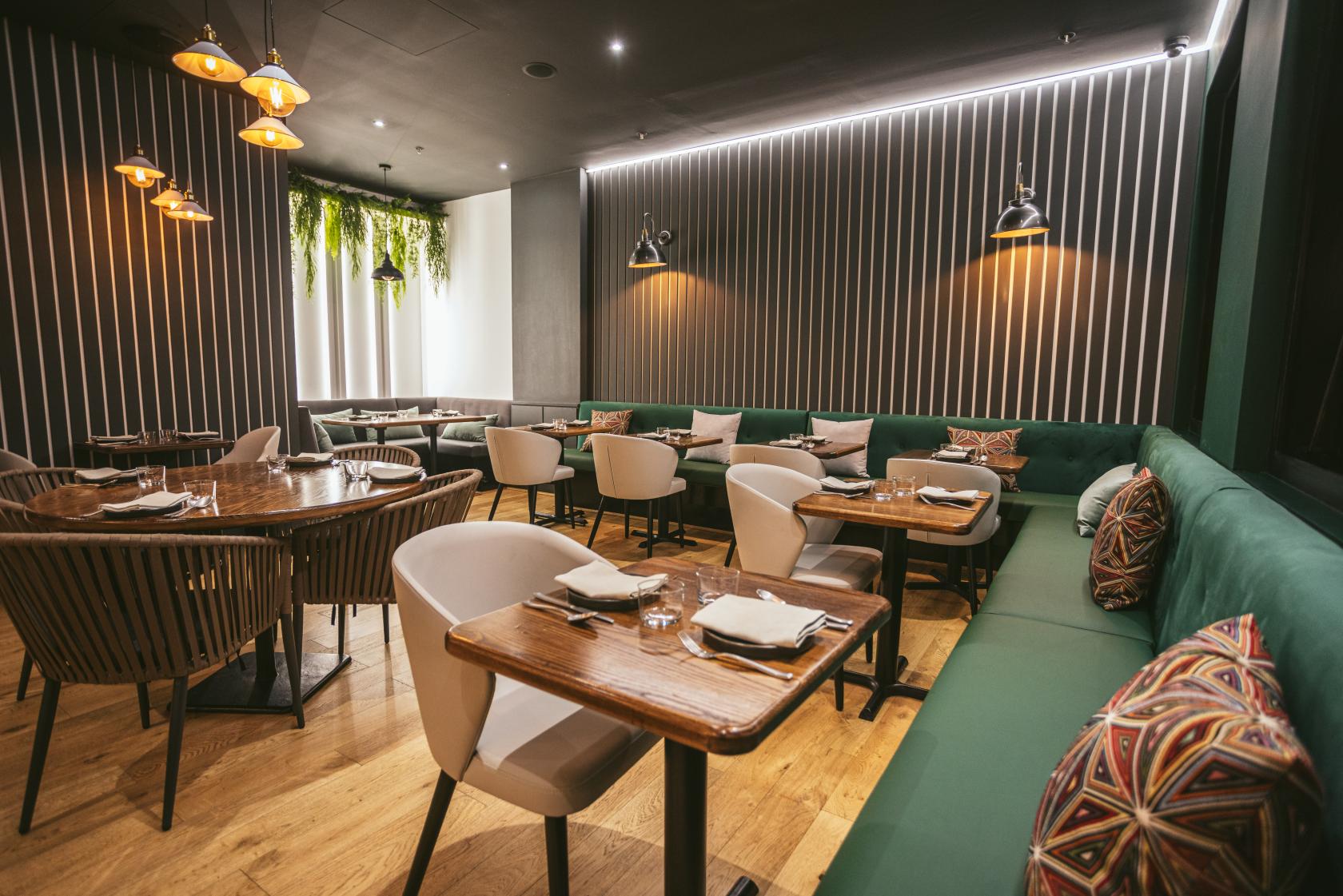 A restaurant dining room with green banquette seating, wood tables, and hanging pendant lights at Chayote.