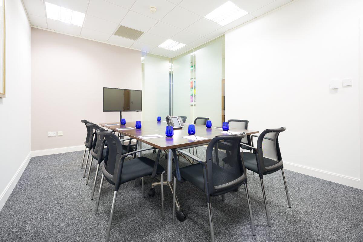 A meeting room with a rectangular table, eight chairs, blue glasses, a TV screen, and glass walls at Landmark: Brindleyplace, Birmingham.