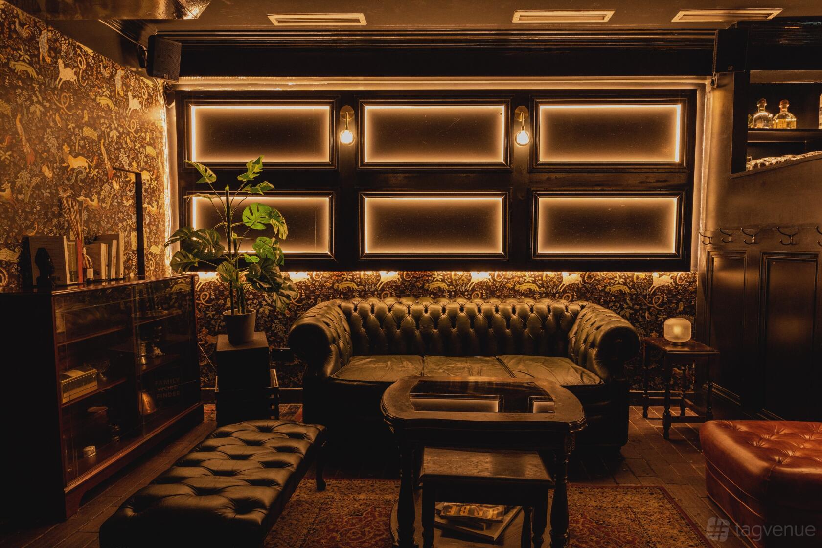 A function room with a leather Chesterfield sofa, patterned wallpaper, and warm ambient lighting at Beasy Soho.