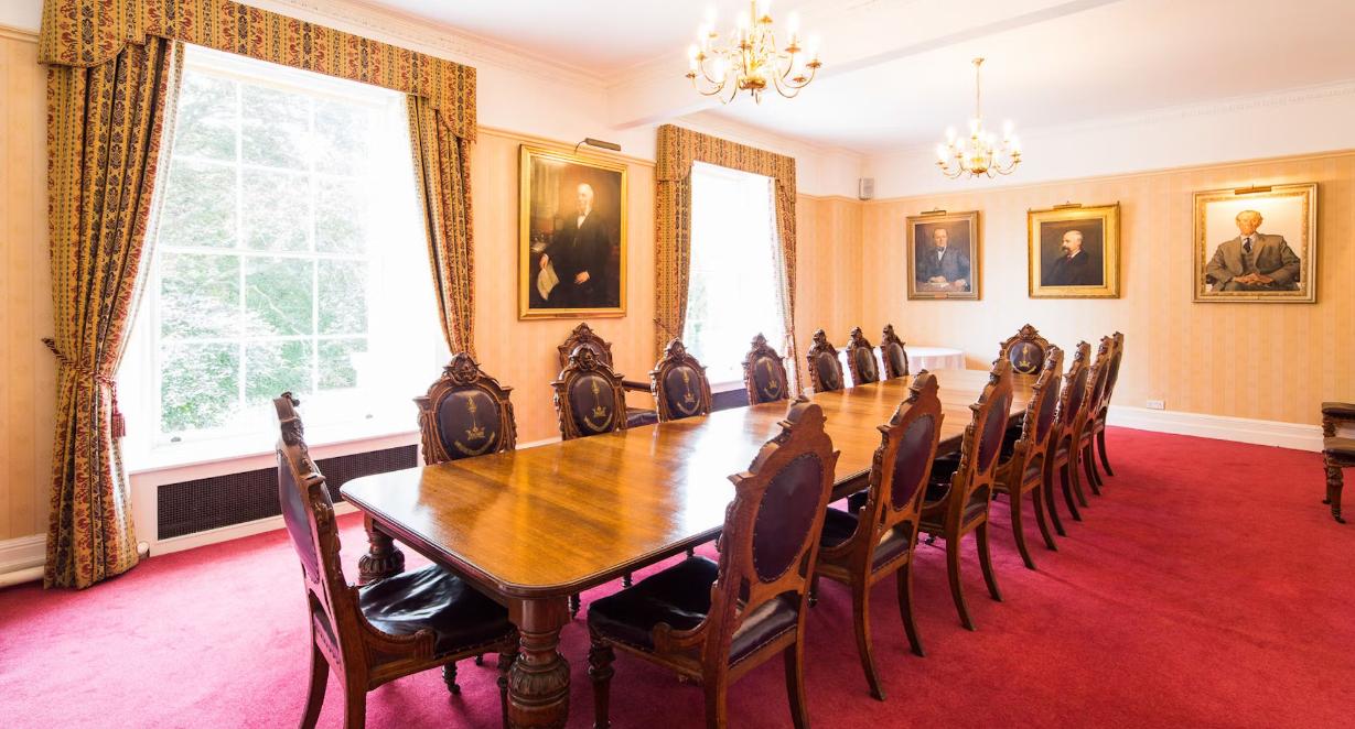 A hall with a long polished wood conference table, antique chairs, chandeliers, and portrait paintings at Merchants' Hall.