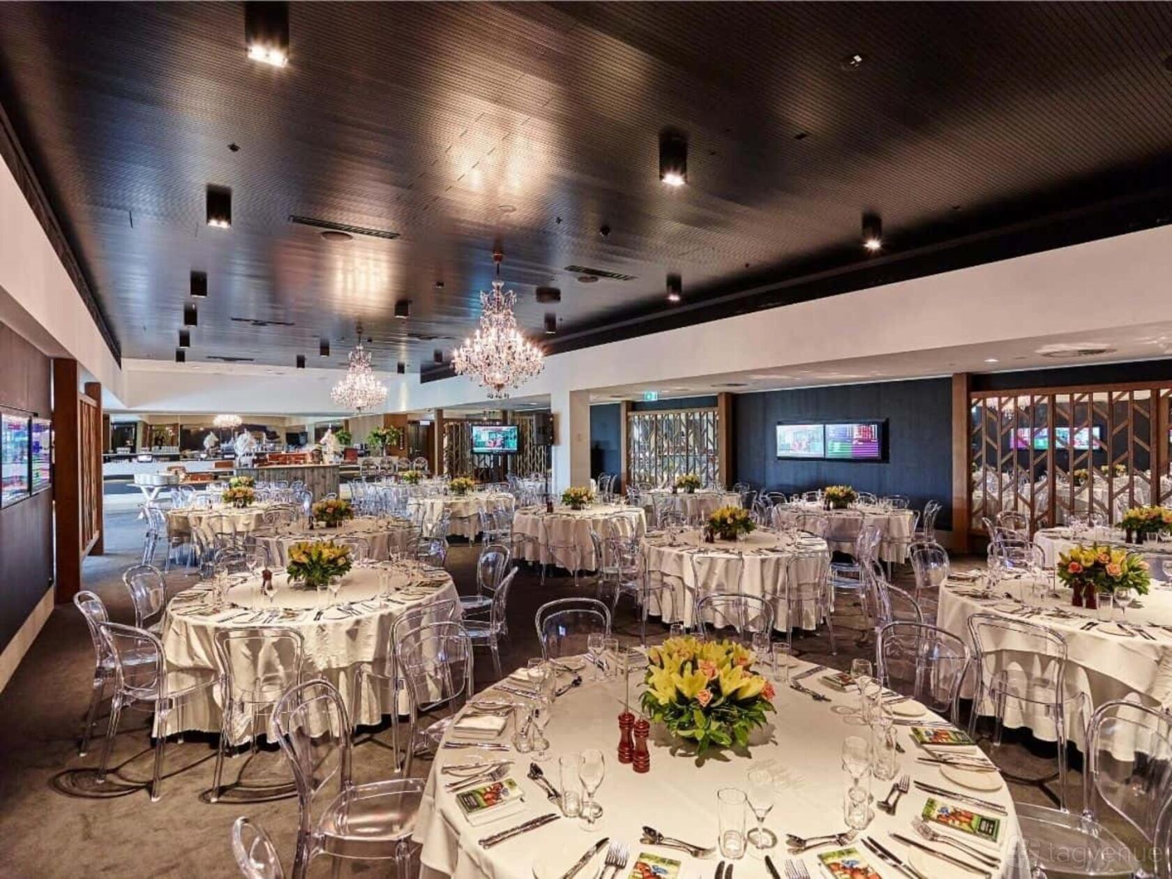 A banquet hall with chandeliers, round tables with white linens, and clear chairs at Australian Turf Club @ Royal Randwick.