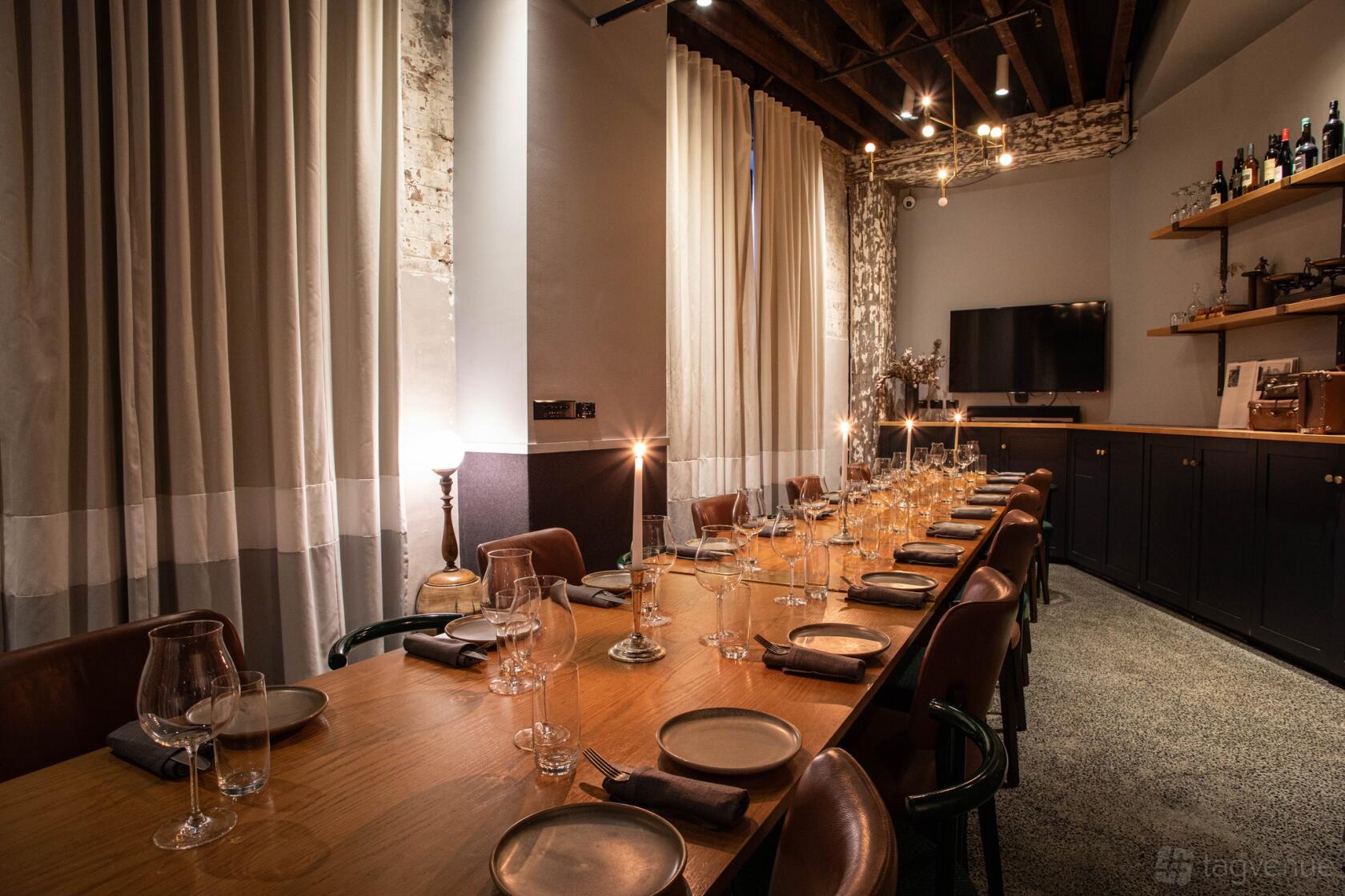 A dining room with a long wooden table, leather chairs, exposed beams, and candle lighting at PERCY.