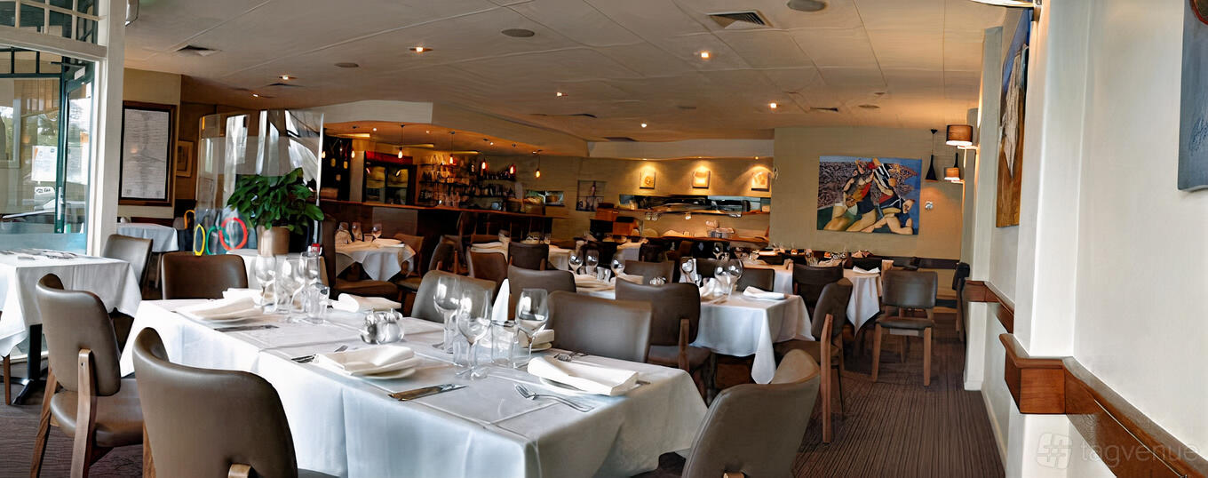 A dining room with white tablecloths, dark chairs, and framed art on the wall at IL Duca Restaurant.