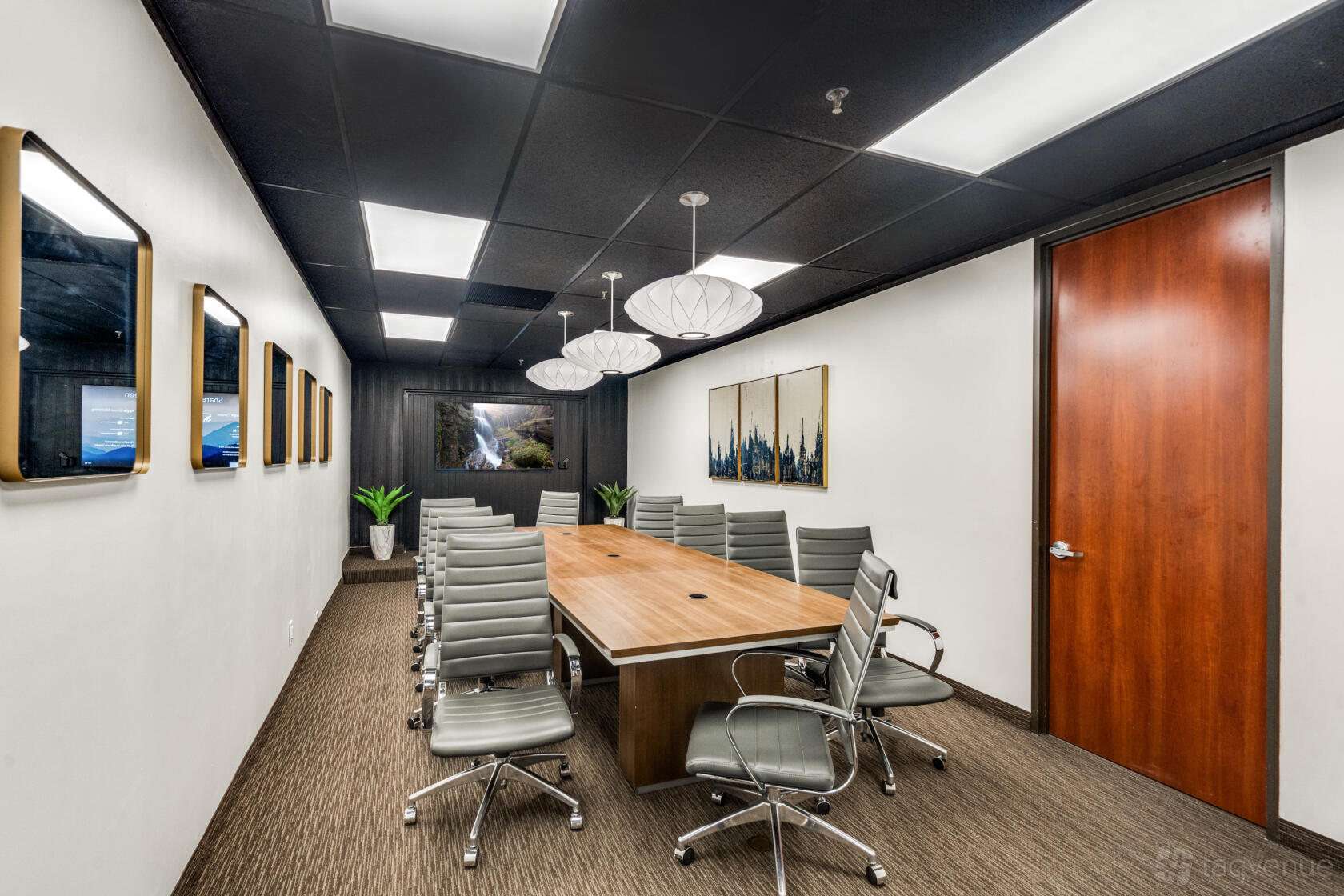 A coworking boardroom with a long wooden table, modern gray chairs, large wall art, and pendant lighting at Lucid Private Offices - LBJ Freeway.
