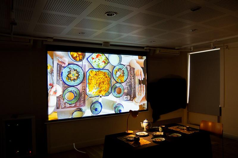A screening room with a large projection screen, dimmed lighting, and a desk with plates at Pushkin House.