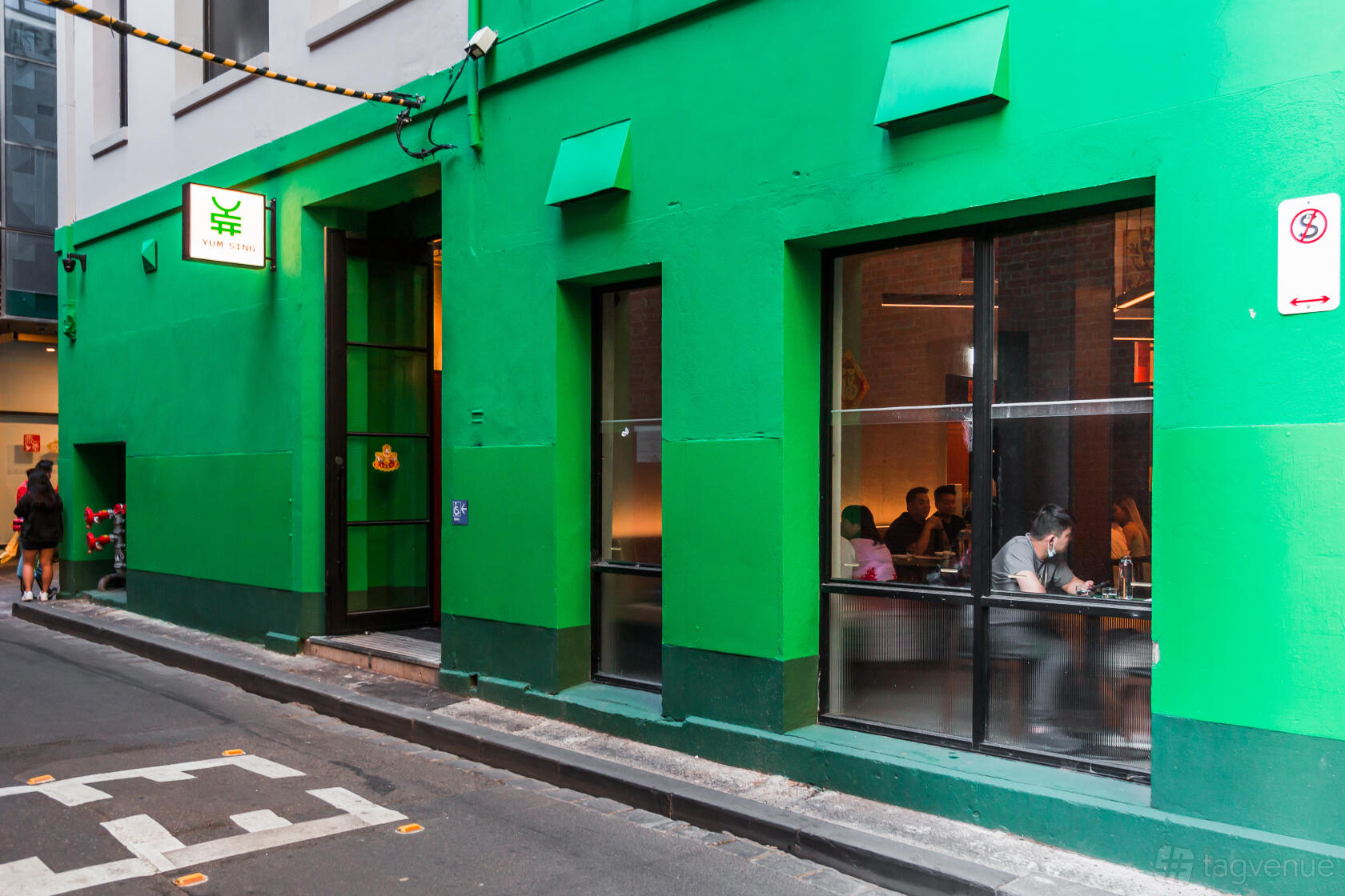 A pub with a bright green exterior, large street-facing windows, and indoor seating visible at Yum Sing House.