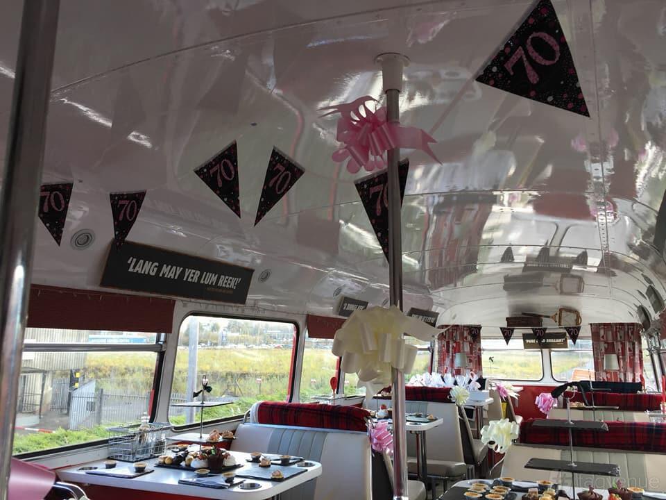 A restaurant set inside a vintage double-decker bus with tartan seating and decorated tables at The Red Bus Bistro Glasgow.