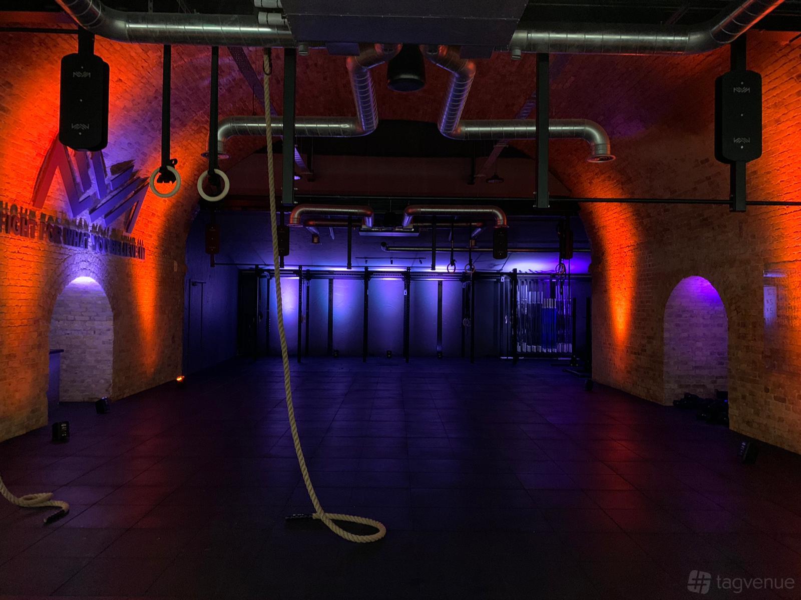 An event space with exposed brick arches, hanging ropes, and colored LED lighting at CrossFit Putney.