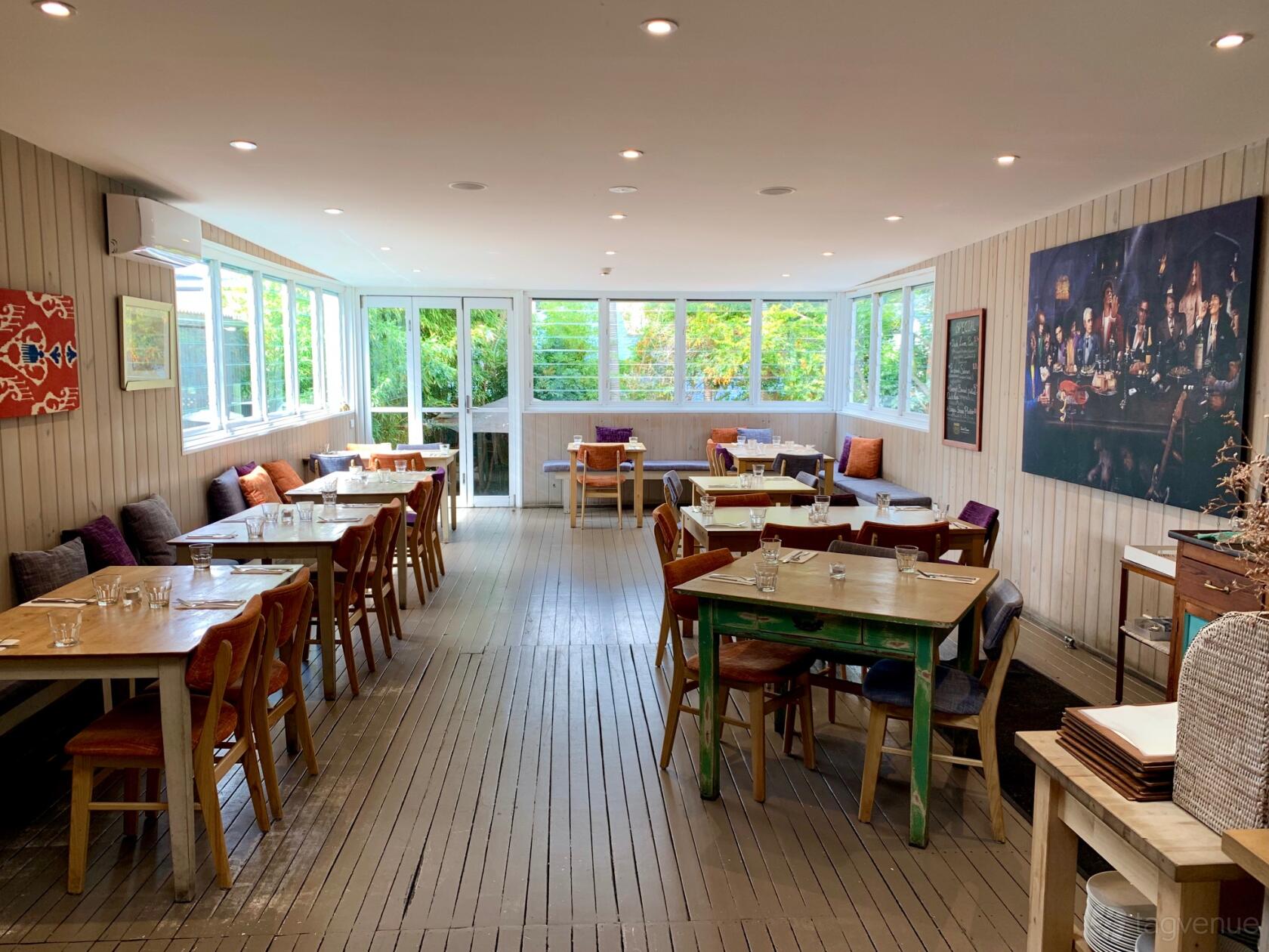 A function room with floor-to-ceiling windows, wooden tables, and colorful cushions at The Duck Inn.