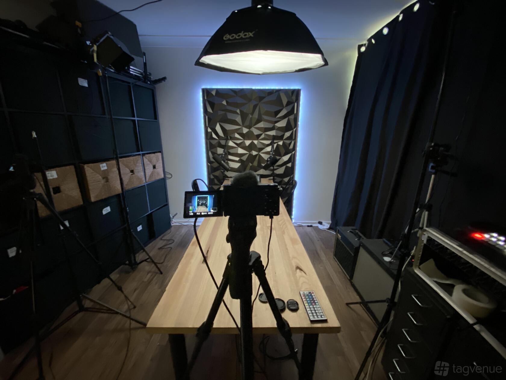 A podcast studio with a central wooden table, soundproofing panels, video camera, and overhead lighting at Beat Tank Productions.
