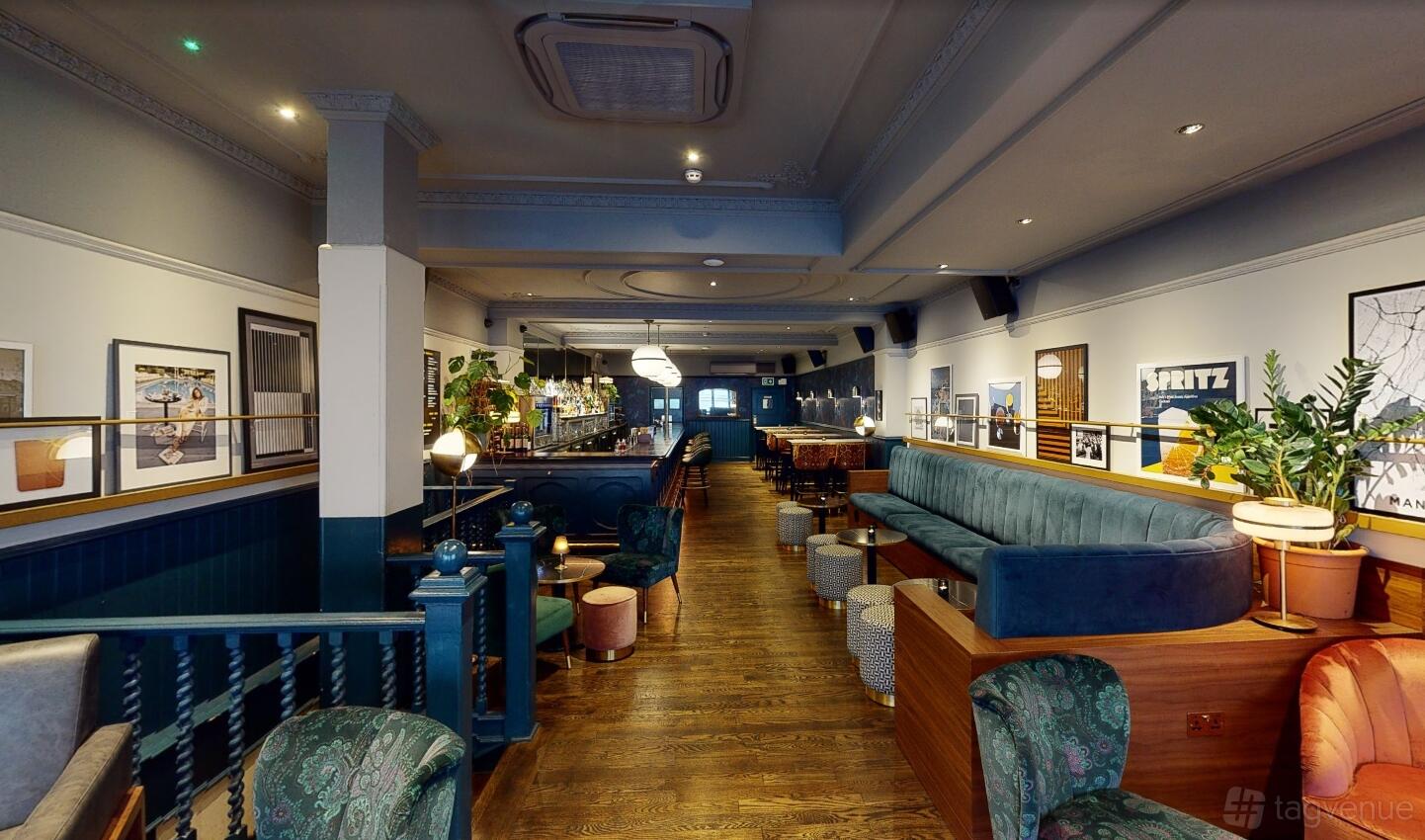 A cocktail bar with velvet banquette seating, framed artwork, and a long wooden floor at LOCKES Bar Covent Garden.