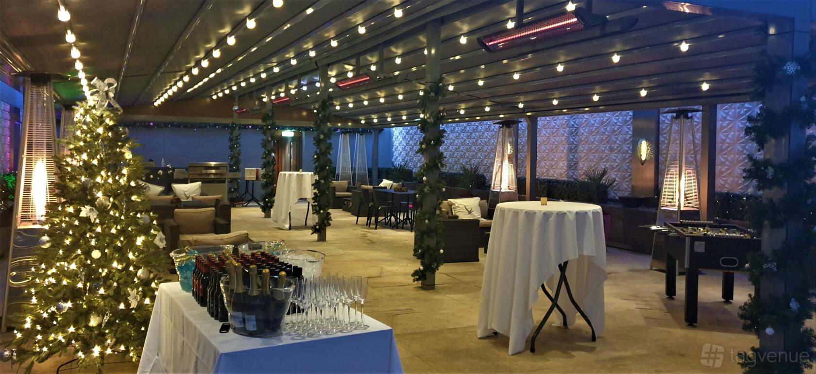 A covered terrace with string lights, cocktail tables with white linens, and lounge seating at The Place Hotel.